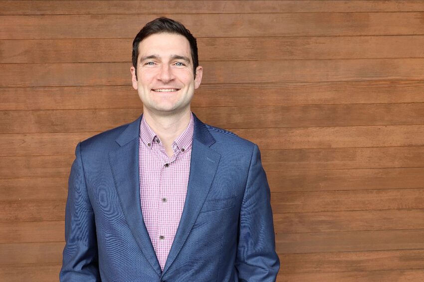 A man in a suit against a wood backdrop.