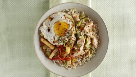 Bowl of rice topped with flaked Alaska salmon, a sunny-side-up egg, shredded vegetables, pickles, and crispy strips, garnished with green onions and chili flakes.