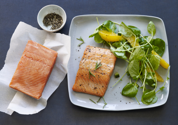 frozen salmon piece sits on parchment paper next to cooked salmon on dinner plate with salad