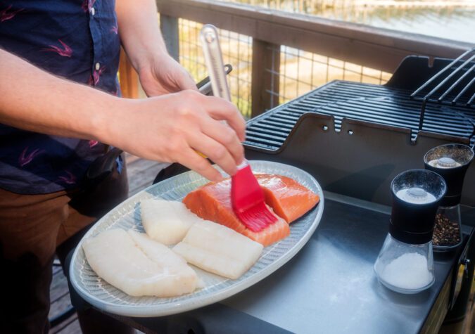 white fish and salmon pieces sitting on plate next to grill outdoors with harbor in background