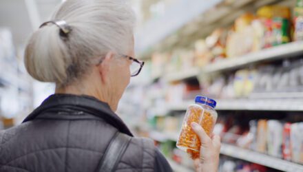 View of back of woman's head who is holding bottle of pills in grocery aisle