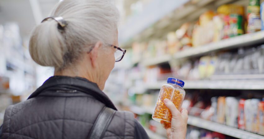 View of back of woman's head who is holding bottle of pills in grocery aisle