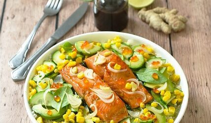Two Wild Alaskan salmon fillets lie on a bed of cauliflower rice. They are surrounded by corn, cucumber, avocado, salmon roe, and baby spinach.