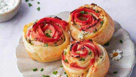 A trio of delicate buds of Alaska smoked salmon surrounded by flaky puff pastry sit on a white plate with a hearty garnish of chives.
