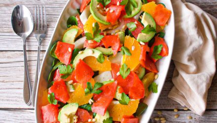bright orange and red salmon slices stand out against green avocado and cilantro on a white plate