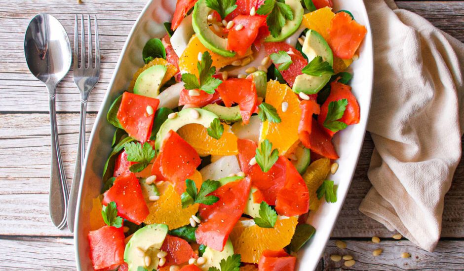 bright orange and red salmon slices stand out against green avocado and cilantro on a white plate