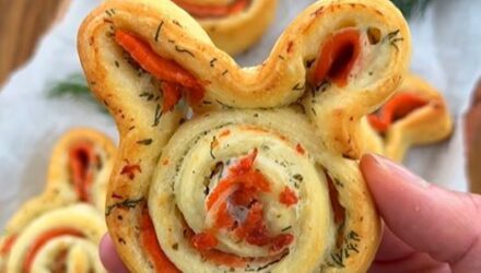 A hand holds a pastry bunny with layers of salmon and herbs. More bunnies are in the background