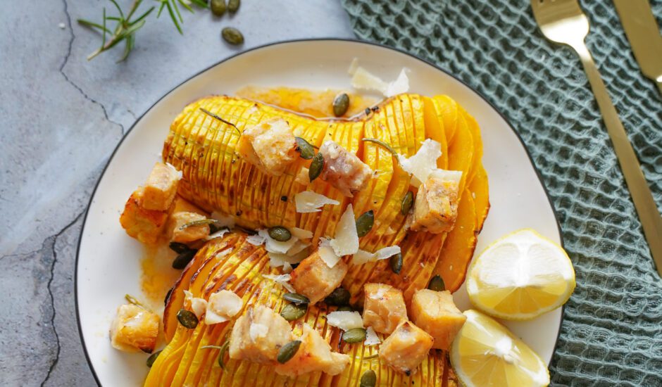 Rosemary Hasselback Butternut Squash Loaded with Honey-Lemon Alaska Cod recipe on white plate against blue napkin and fall decor