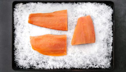Three salmon fillets on a tray of ice.