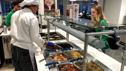 Chef in white hat serves seafood to blond female college student