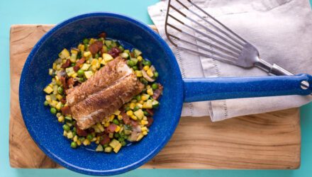 Browned fish on top of corn inside of vibrant blue pan on wood and teal background