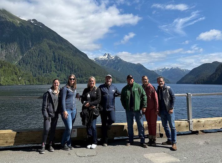 Smiling group of people on tour with Alaska mountains and ocean in backgroung
