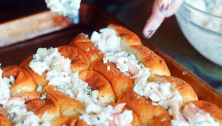 hands with nail polish reach for tray of rolls stuffed with seafood