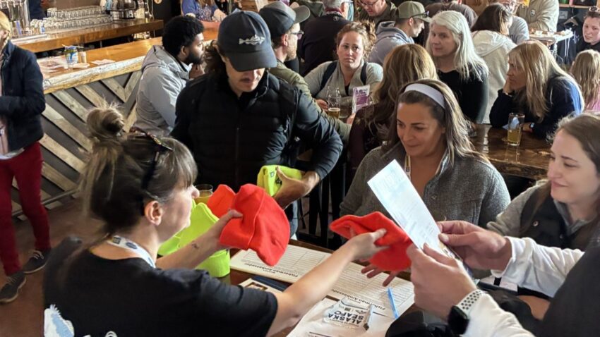 A lady hands out knit beanie hats to a packed room. 