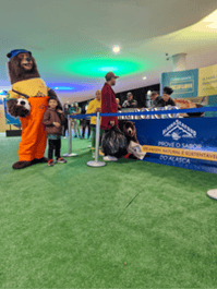 brown bear mascot holding a soccer ball waiting in line for Alaska Seafood table with samples.