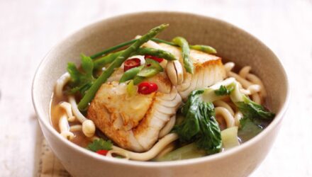 white fish with greens over udon noodles in white bowl with white spoon